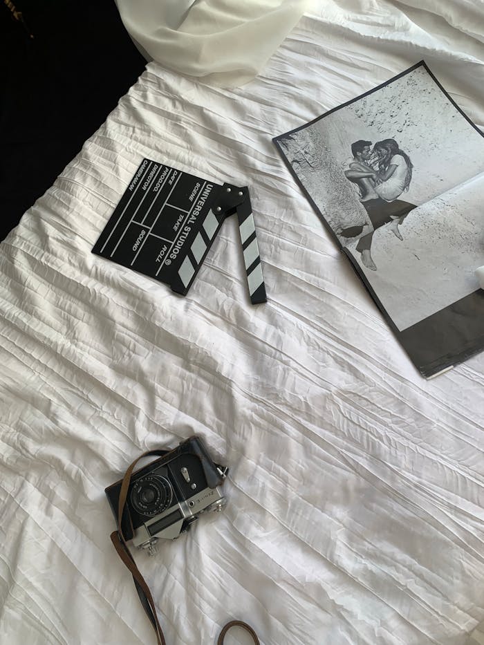 Black and white photo with vintage camera and film slate on a white sheet bed.